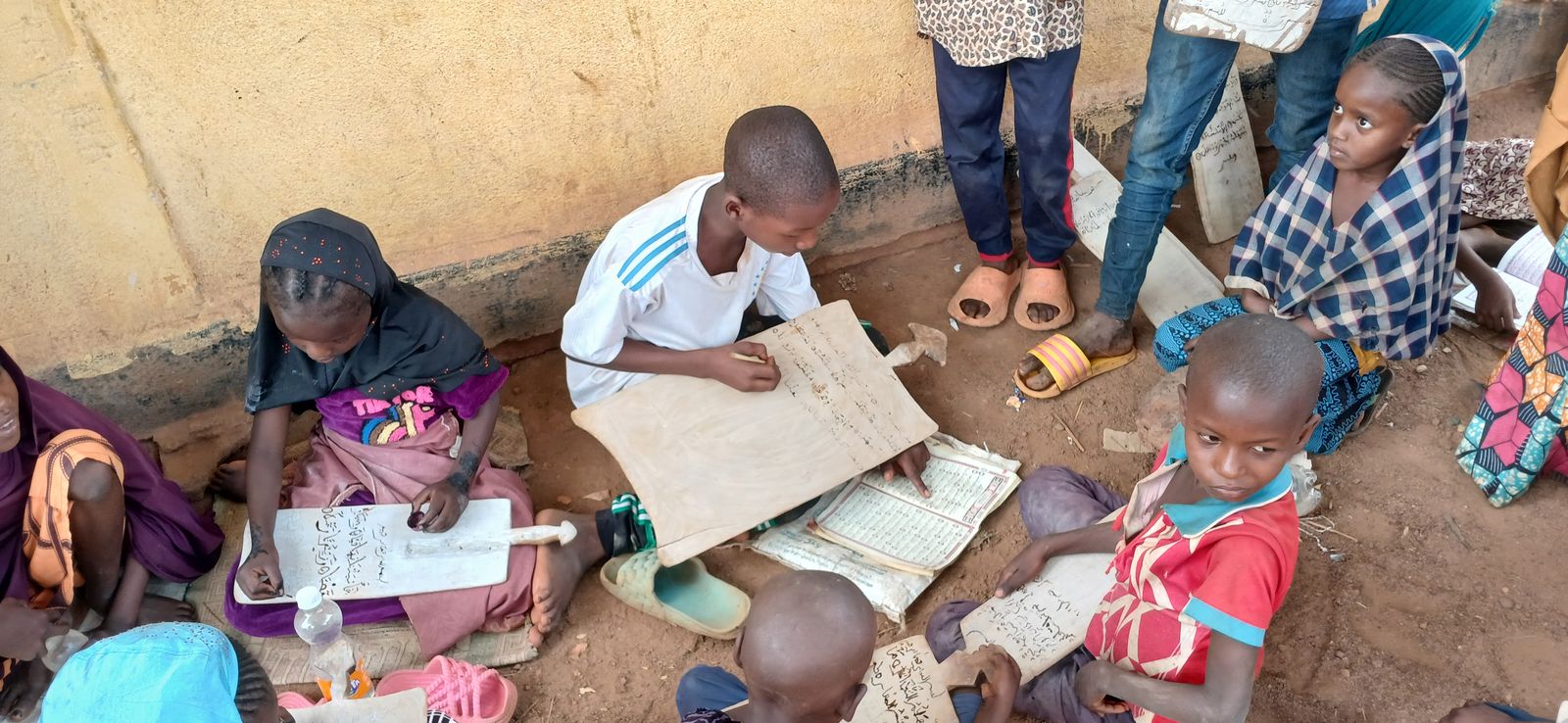 Children studying Quran on wooden boards at Lolo Camp, February 2025